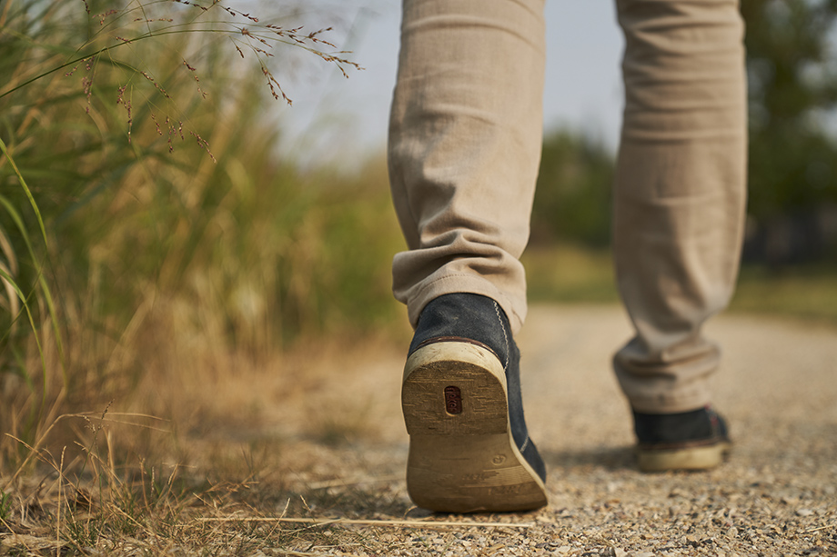 Close up of the feet of a man walking on a gravel trail